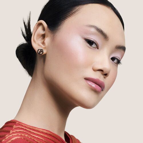 Portrait d'une femme avec des boucles d'oreilles modernes, un maquillage subtil et un haut en satin rouge.