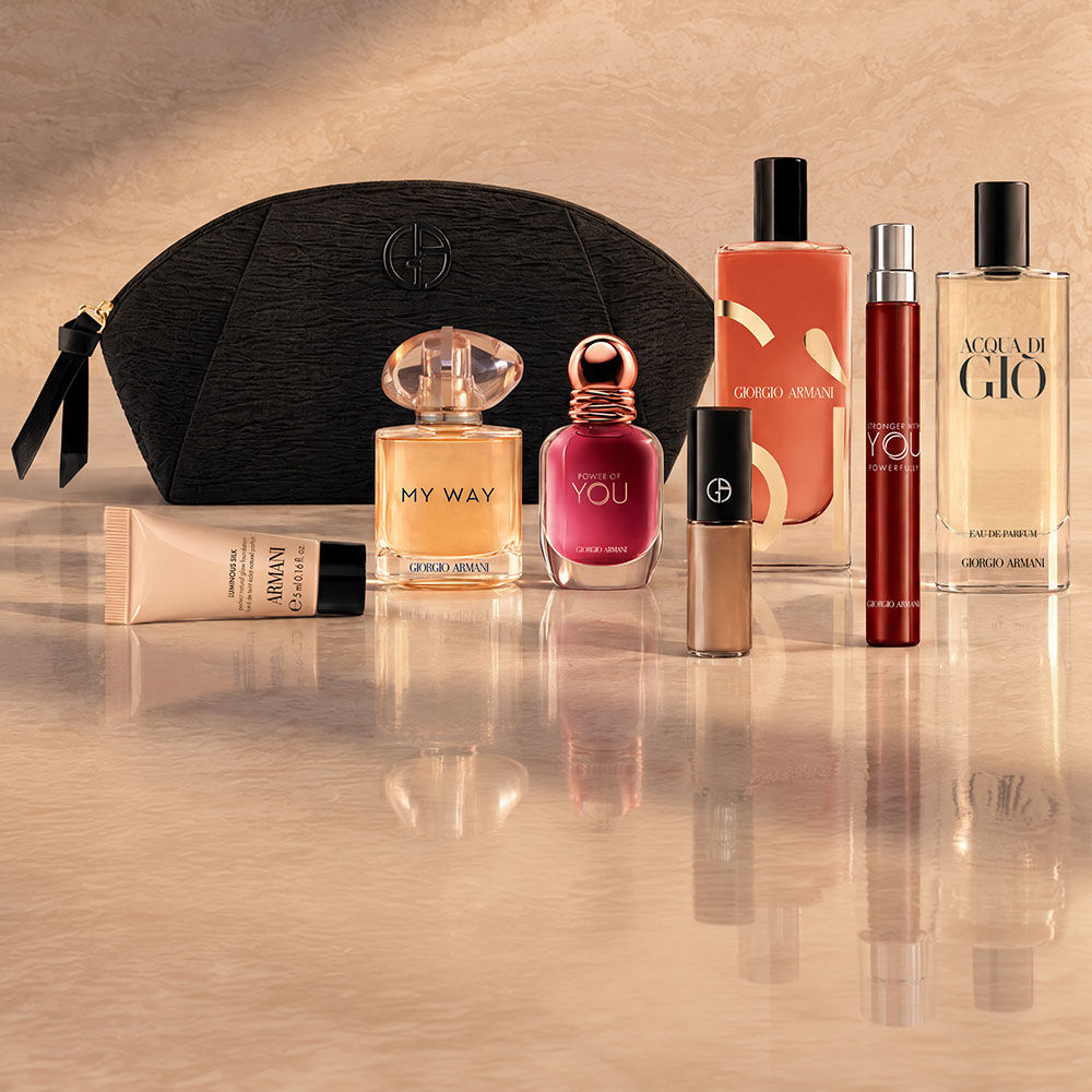 Une pochette noire Armani Beauty accompagnee de parfums, de maquillage et de soins sur un fond beige.