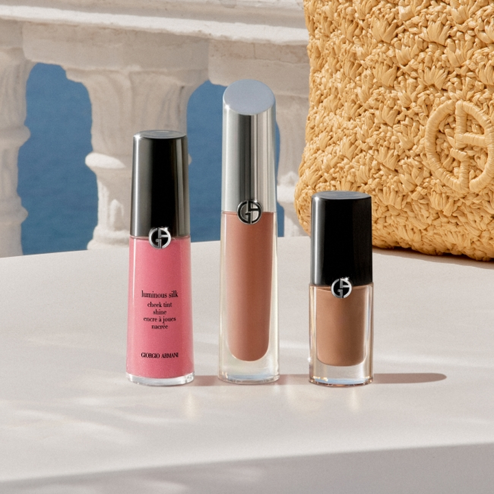 Produits de maquillage Giorgio Armani presentes sur un socle blanc : un blush liquide rose, un gloss nude et un rouge a levres liquide brun, dans un decor d’inspiration mediterraneenne avec des arches en pierre, un ciel bleu et un accessoire dore texture.