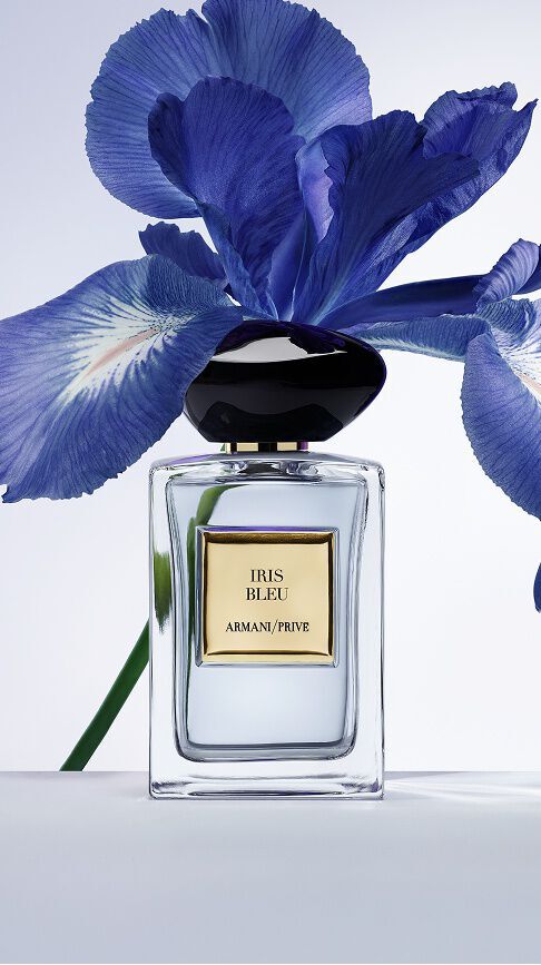 Armani/Prive Iris Bleu : un flacon en verre transparent au capot pierre noire, pose devant un iris bleu vibrant, capturant un equilibre delicat entre elegance florale et profondeur.