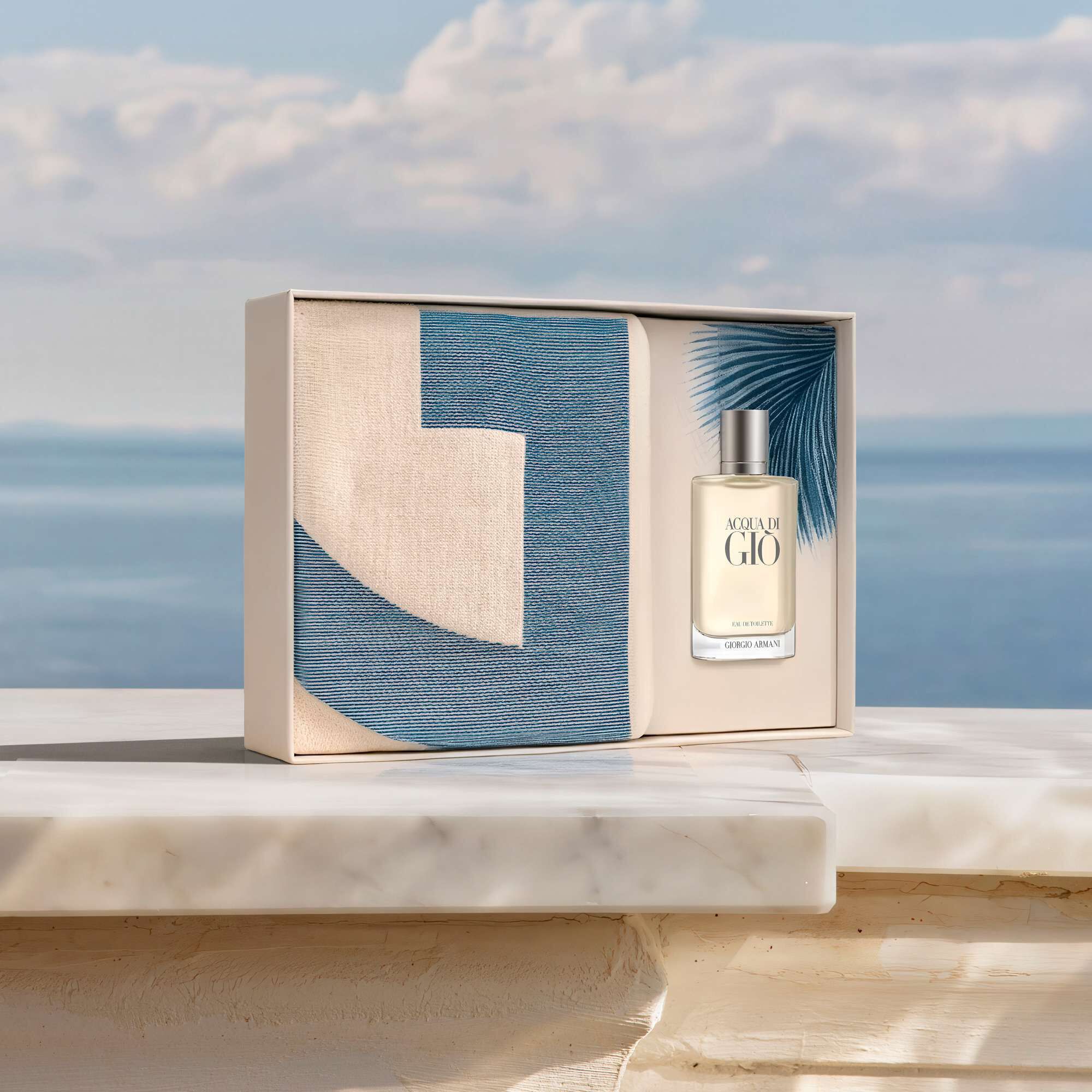 Armani beauty Acqua di Gio Eau de Toilette. The iconic men’s fragrance bottle rests elegantly beside a vintage camera on a blue and white striped canvas, bathed in sunlight. Discover a sophisticated Mediterranean escape.