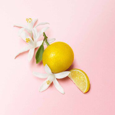 A vibrant yellow lemon and a slice of lemon accompany delicate white flowers on a soft pink background.