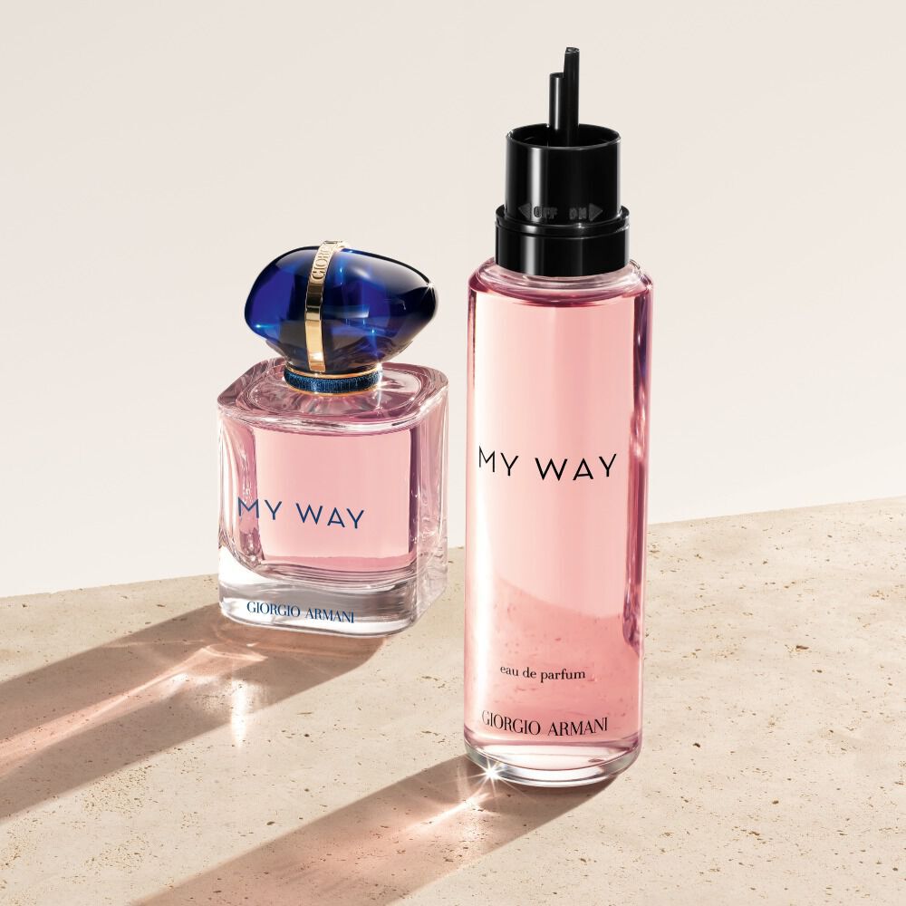 Un flacon et une recharge d'eau de parfum Giorgio Armani My Way. Le flacon original, rose pale avec un bouchon bleu, est place a cote de sa recharge rose translucide, plus haute. Ils reposent sur une surface texturee et pale.