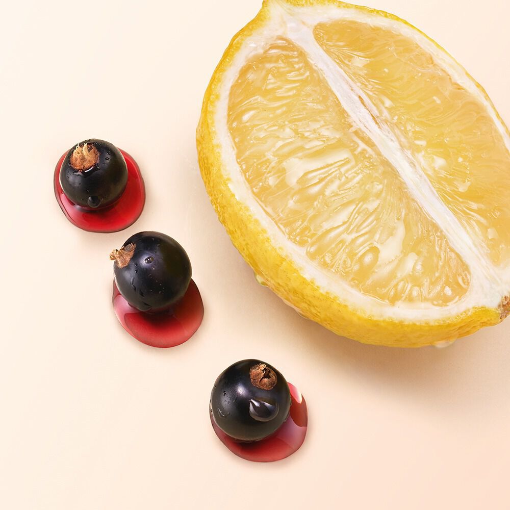 Close-up of a lemon slice with dark berries on a nude background.