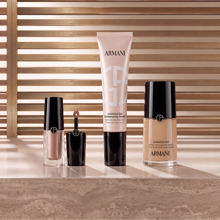Produits de maquillage Armani beauty comprenant un enlumineur liquide, la base illuminatrice Luminous Silk et le fond de teint Luminous Silk disposes sur une surface en marbre devant un fond chaleureux a lattes.