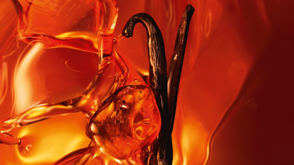 Un gros plan de deux gousses de vanille foncees et de resine d ambre scintillante sur un fond ambre chaud et lumineux.