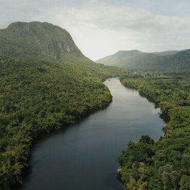 A serene river winds through lush green mountains and dense forest under a cloudy sky.