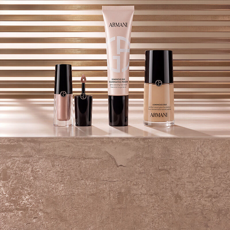 Produits de maquillage Armani beauty comprenant un enlumineur liquide, la base illuminatrice Luminous Silk et le fond de teint Luminous Silk disposes sur une surface en marbre devant un fond chaleureux a lattes.
