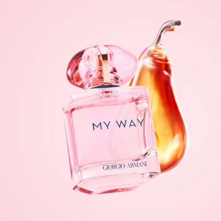 A bottle of pink perfume labeled "MY WAY" by Giorgio Armani, with a pear-shaped element in the background, all set against a soft pink backdrop.