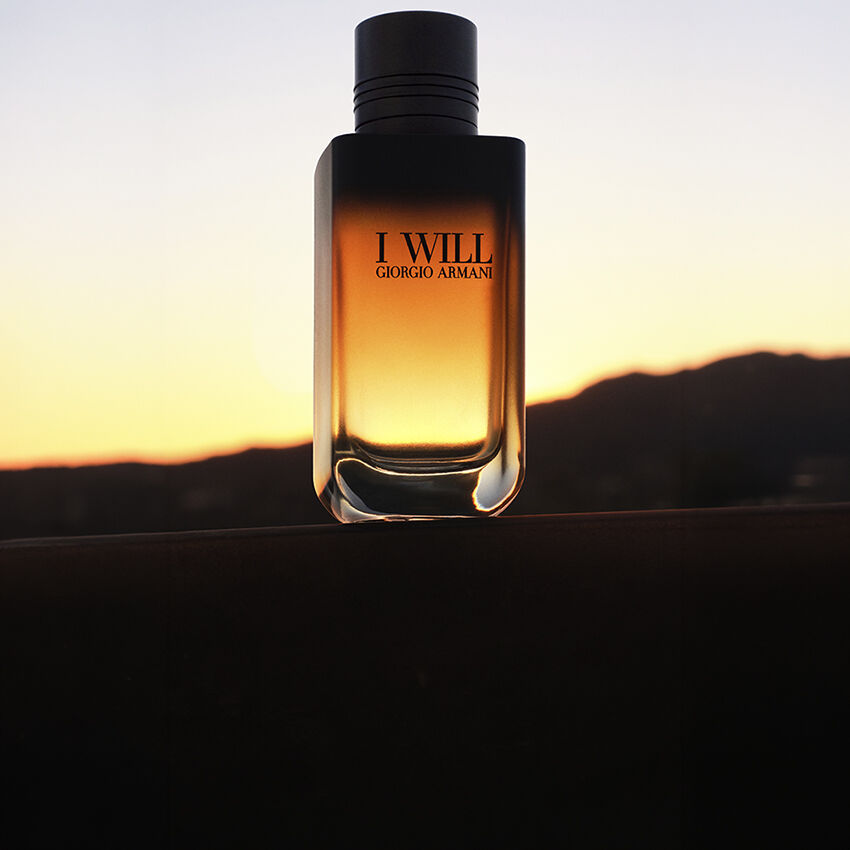 Flacon de parfum I WILL de Giorgio Armani sur fond de paysage au coucher du soleil.