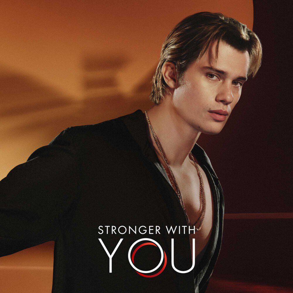 Nicholas Galitzine et le logo Stronger with You, avec le logo Emporio Armani flou derriere lui.