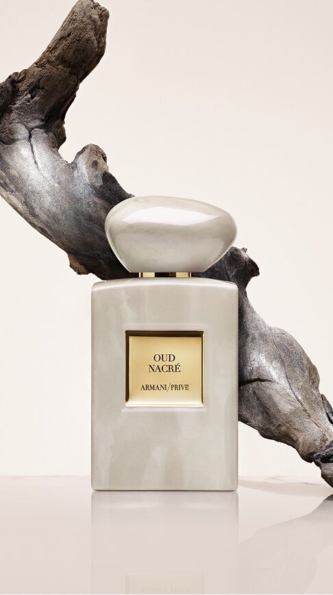 Armani/Prive Oud Nacre: a bottle with pearlescent, iridescent reflections before a piece of sculpted driftwood, capturing the timeless nobility of Oud in a trail of absolute purity and elegance.