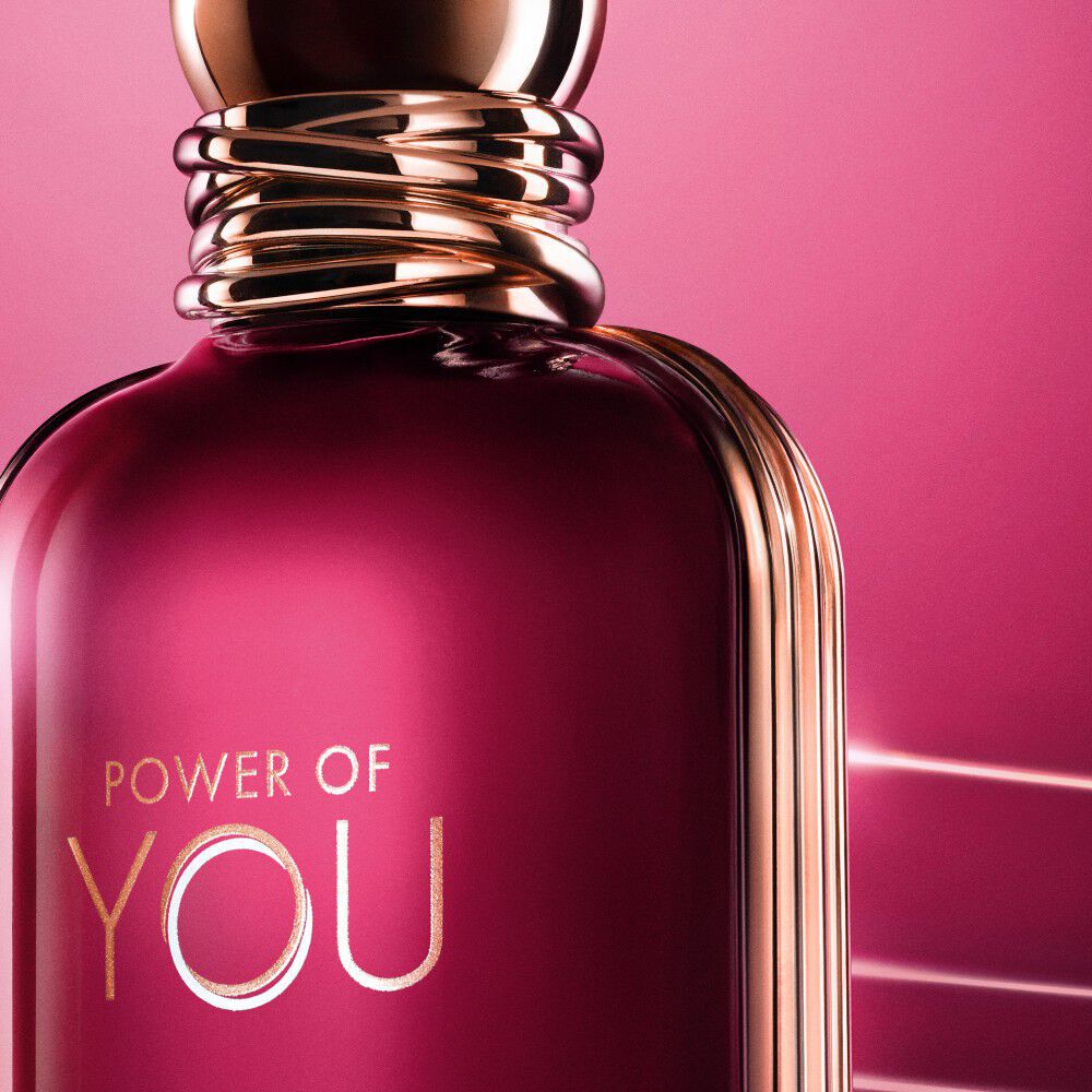 Close-up of the ARMANI POWER OF YOU perfume bottle, glowing in radiant ruby tones with sleek gold accents.