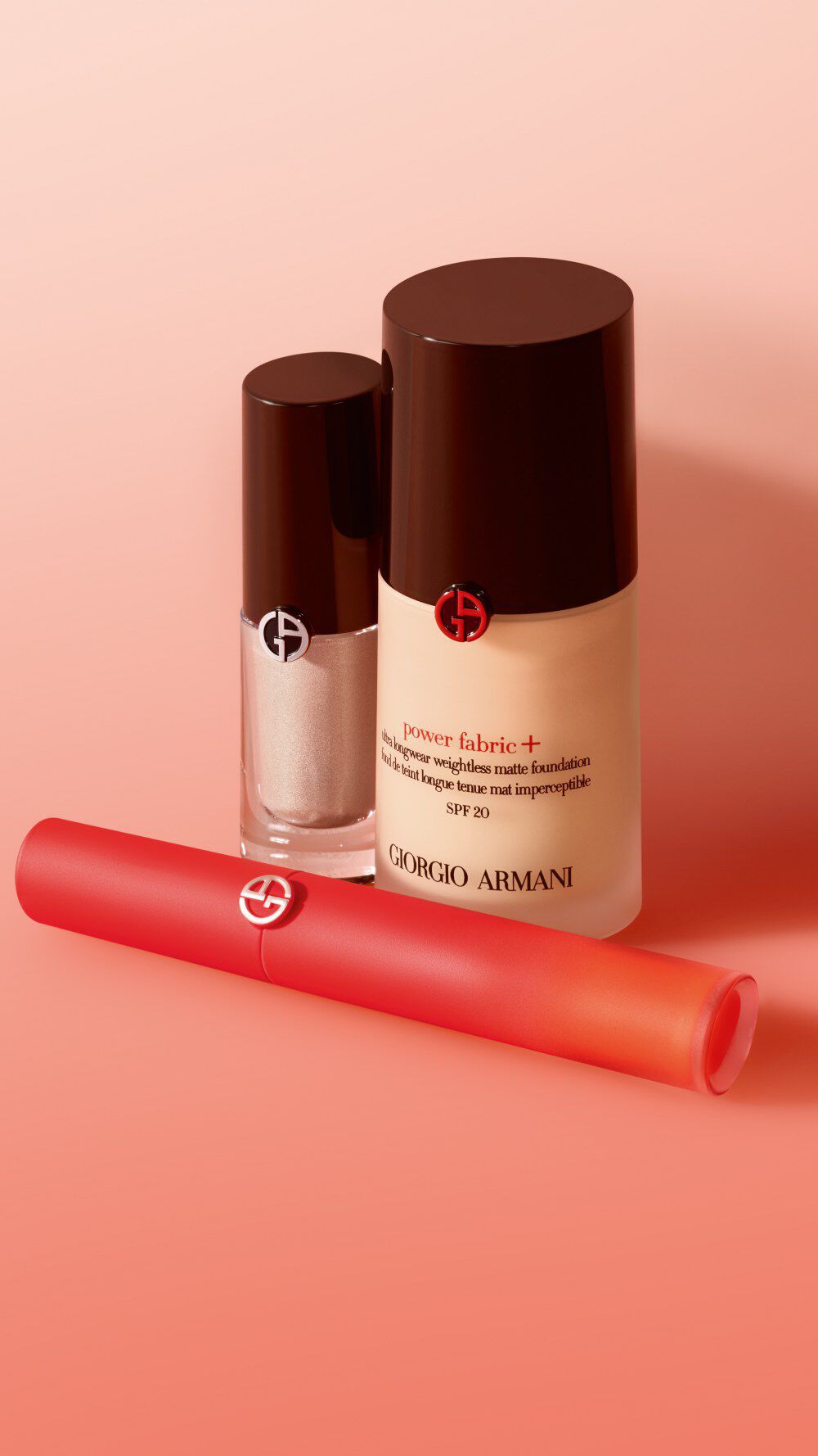 A flat lay of Giorgio Armani beauty products, including a foundation bottle, a primer, and a lip product, all against a soft gradient background.