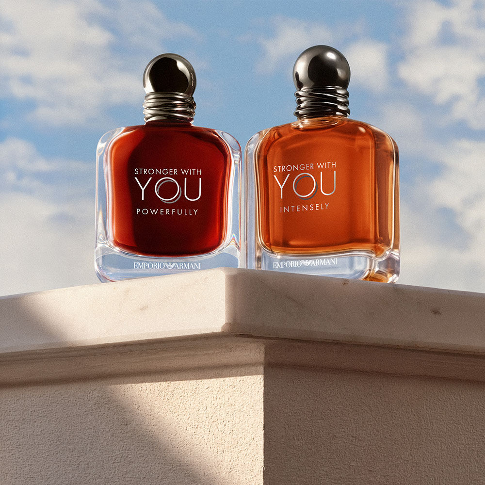 es fragrances Stronger With You Powerfully et Stronger With You Intensely d’Emporio Armani, presentees sur un socle en pierre sous un ciel bleu.​