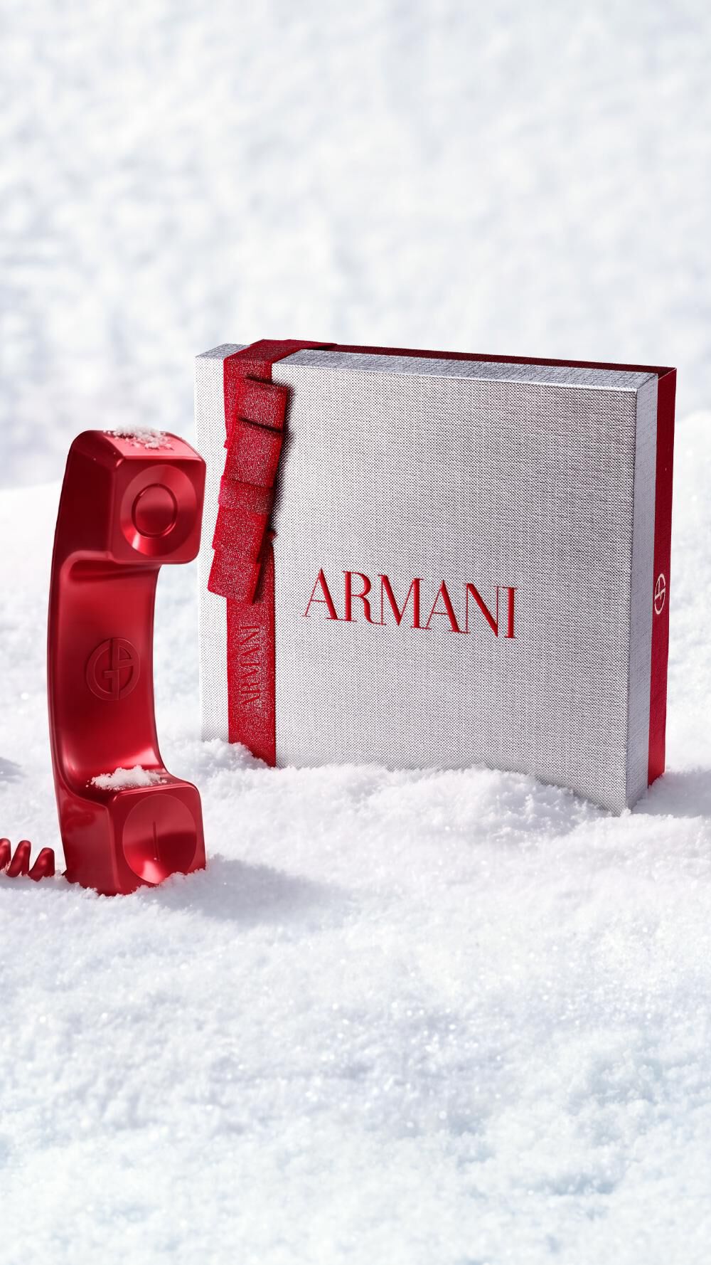 Coffret cadeau de Noel Armani Beauty accompagne d’un telephone rouge evoquant le service client, dans un decor enneige.