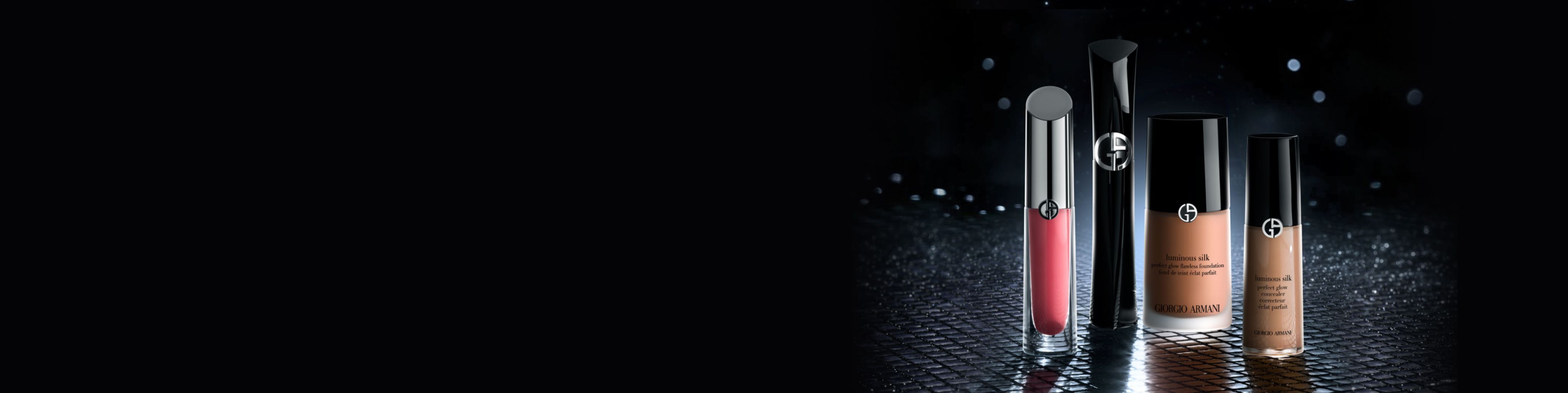 Maquillage Armani Beauty sur fond sombre : laque a levres rouge, mascara noir, fond de teint Luminous Silk et correcteur sur surface reflechissante.