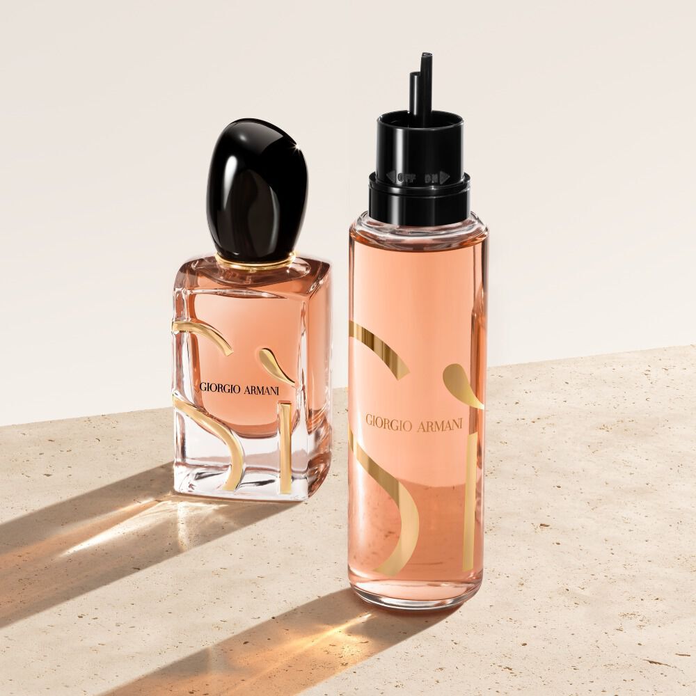 Deux flacons d'eau de parfum Giorgio Armani Si reposent sur une surface beige. Le flacon de gauche est le flacon classique du parfum Si, tandis que celui de droite est une recharge a l'aspect plus translucide et peche.
