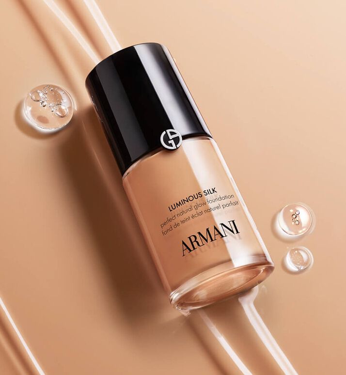 Image Armani Luminous Silk foundation bottle in beige packaging surrounded by dewdrops on a golden beige background.