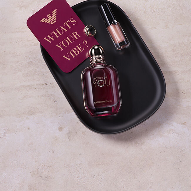 Emporio Armani Power of You fragrance bottle and metallic lip colour on a black tray, alongside a card reading “What’s Your Vibe?”.