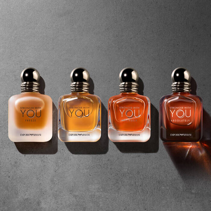 A flat lay of four bottles of "Stronger With You" fragrances by Emporio Armani, showcasing different colors and designs against a dark, textured background.