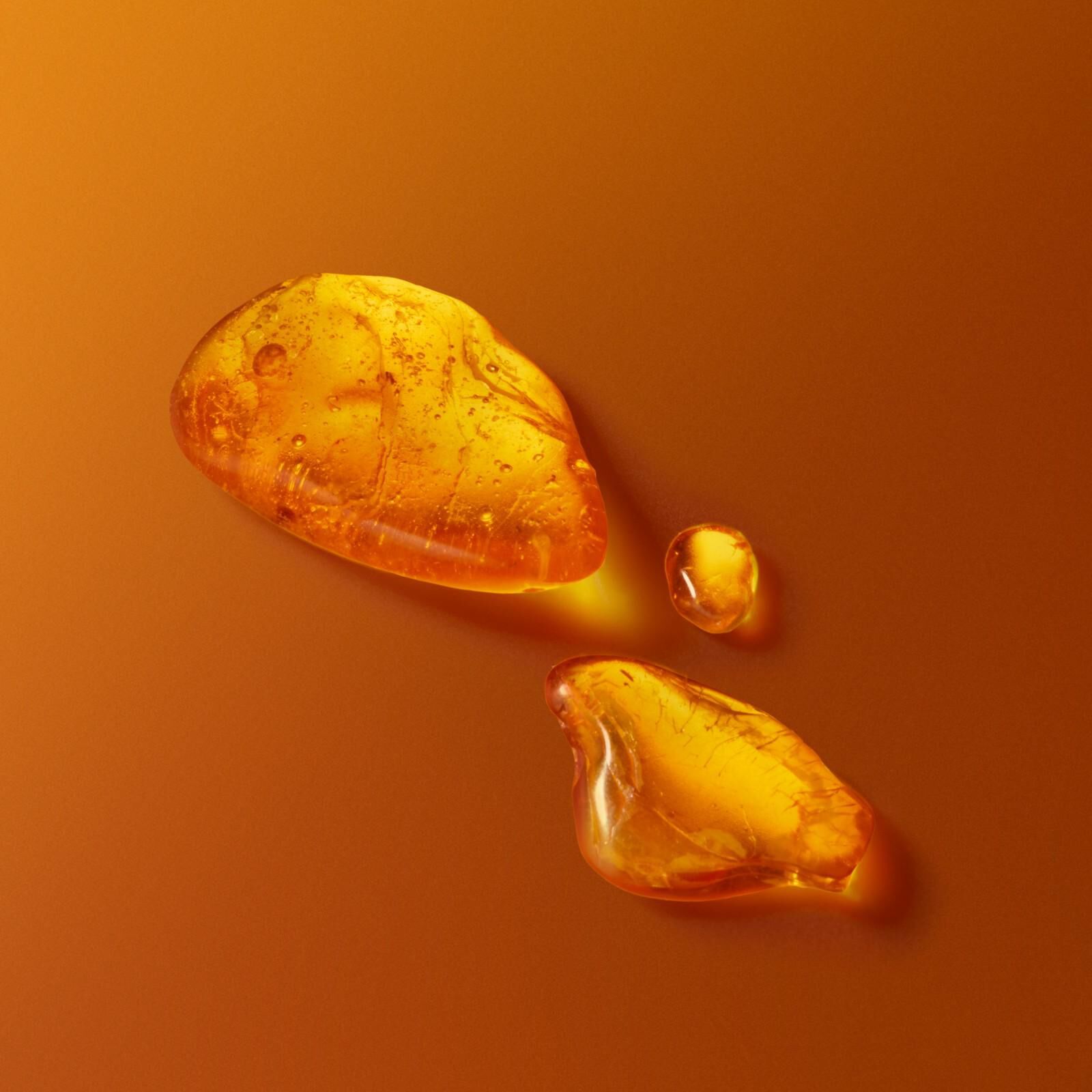 Gouttelettes d'ambre dore et morceaux de resine sur fond orange chaud representant l'essence du parfum.