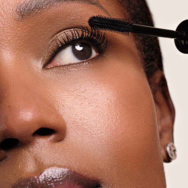 Close-up of a model applying Giorgio Armani Vertigo mascara in Obsidian Black to upper lashes with the mascara wand, showcasing defined and lengthened lash results.
