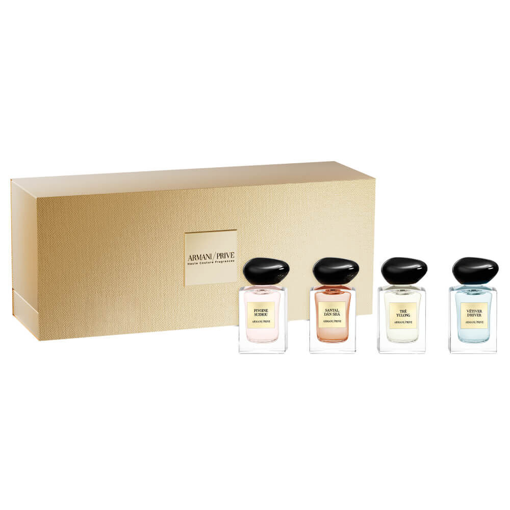 Armani Prive Les Eaux Holiday gift set on white background: gold rectangular box with four miniature eau de parfum bottles with black caps arranged beside it.
