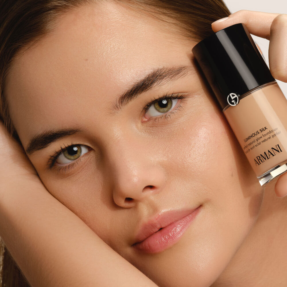 A model holding a Giorgio Armani LUMINOUS SILK FOUNDATION bottle, emphasizing its natural radiance.
