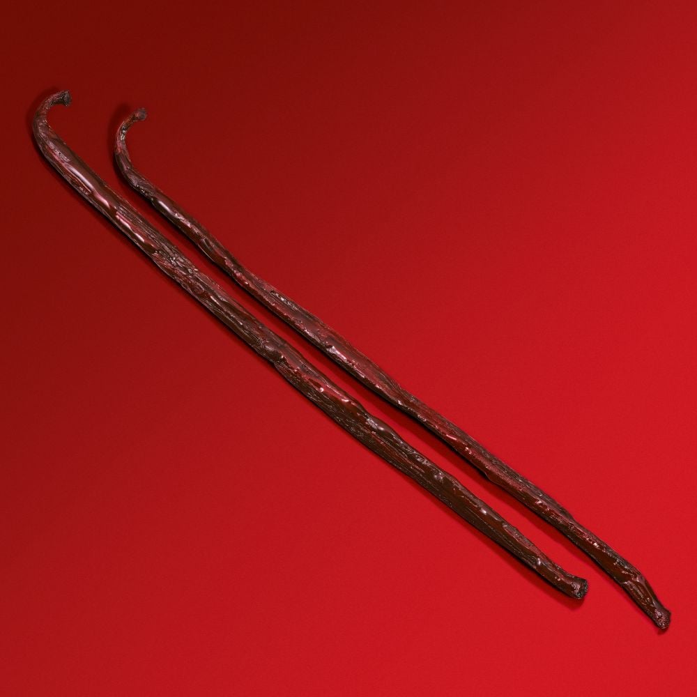 Deux bâtons ondulés en bois, posés sur un fond rouge, montrant une surface texturée et des extrémités courbées.