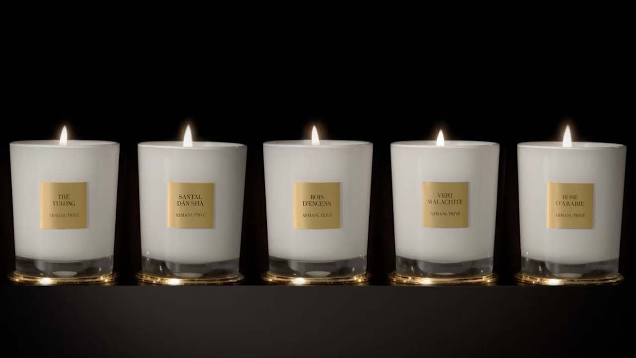 Cinq bougies parfumées allumées sur un fond noir, chacune dans un verre avec une étiquette dorée.