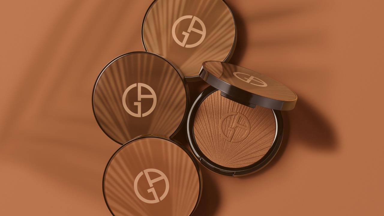 Four compacts of bronzer by Giorgio Armani are arranged on an earthy brown background, highlighting their elegant design.